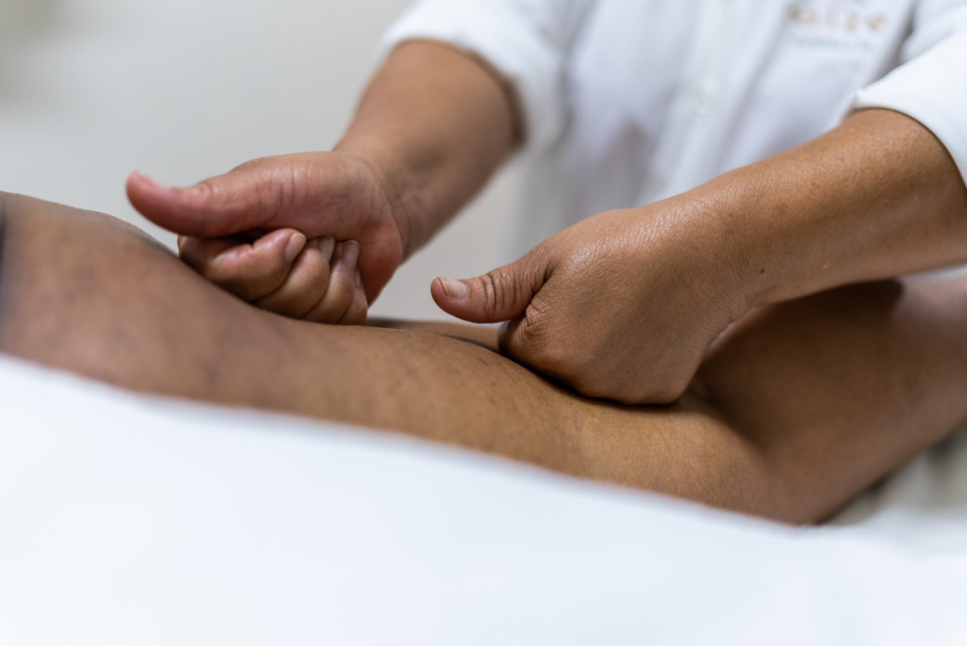 A person performs a therapeutic massage on another person's arm, focusing on pressure points, in a calming, professional setting with white linens.