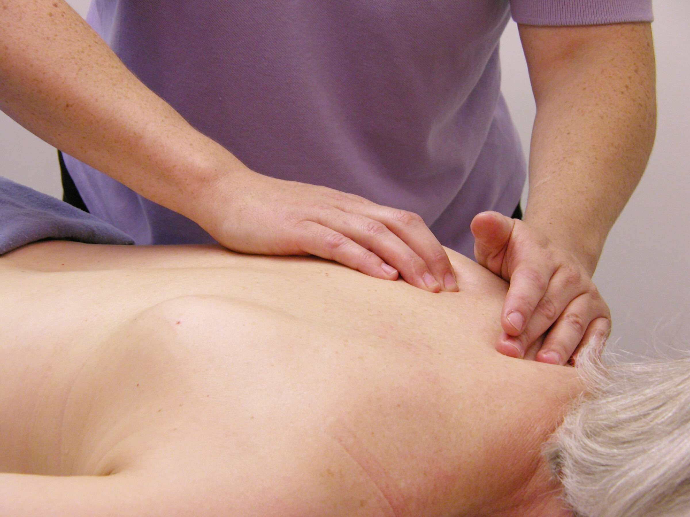 A person receives a massage in a calm setting. Focused hands apply pressure on the back, while the recipient lies relaxed, hair gently laid down.