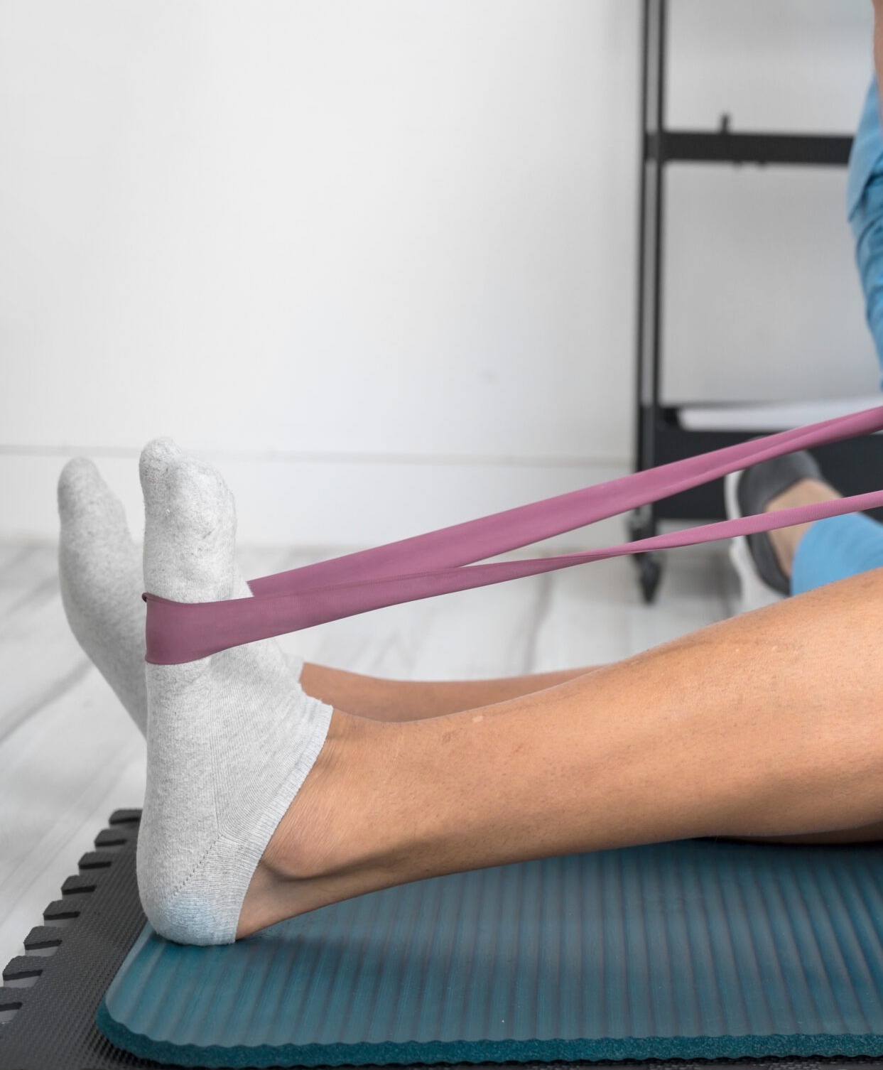 A person stretching on a yoga mat with a resistance band and socks, in a minimal home exercise setting.