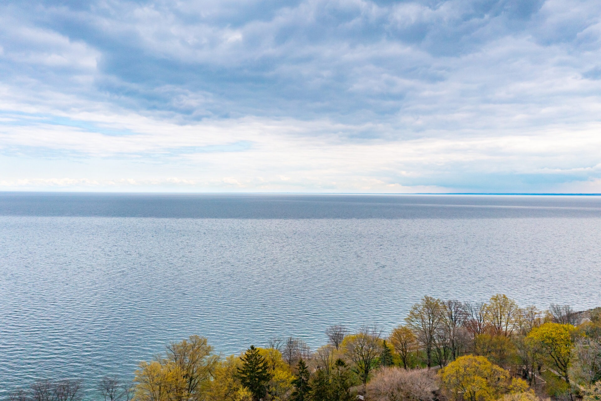 Calm lake view with partly cloudy sky, surrounded by trees with autumn foliage in various colors. No landmarks or historical buildings visible.