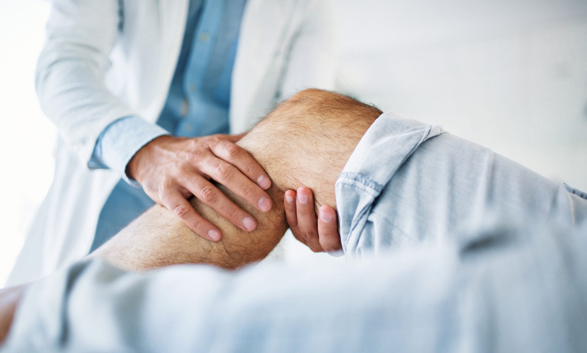 A person in a medical setting examines another person’s bent knee, focusing on assessing joint movement or injury in a close-up view.